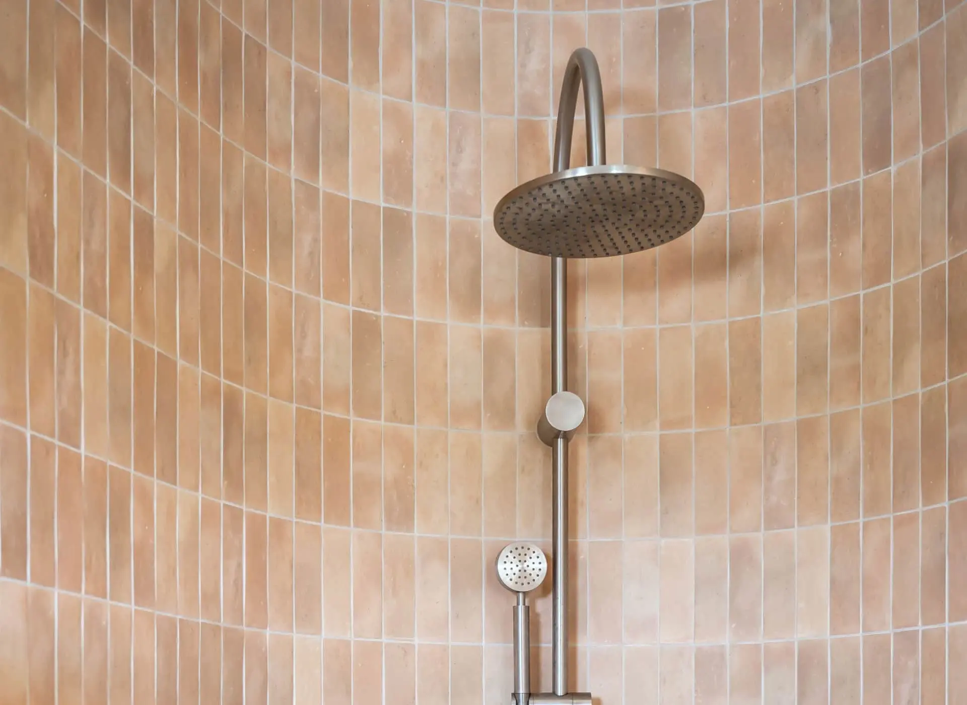 Modern rainfall shower head with handheld attachment mounted on peach-colored tiled shower wall.