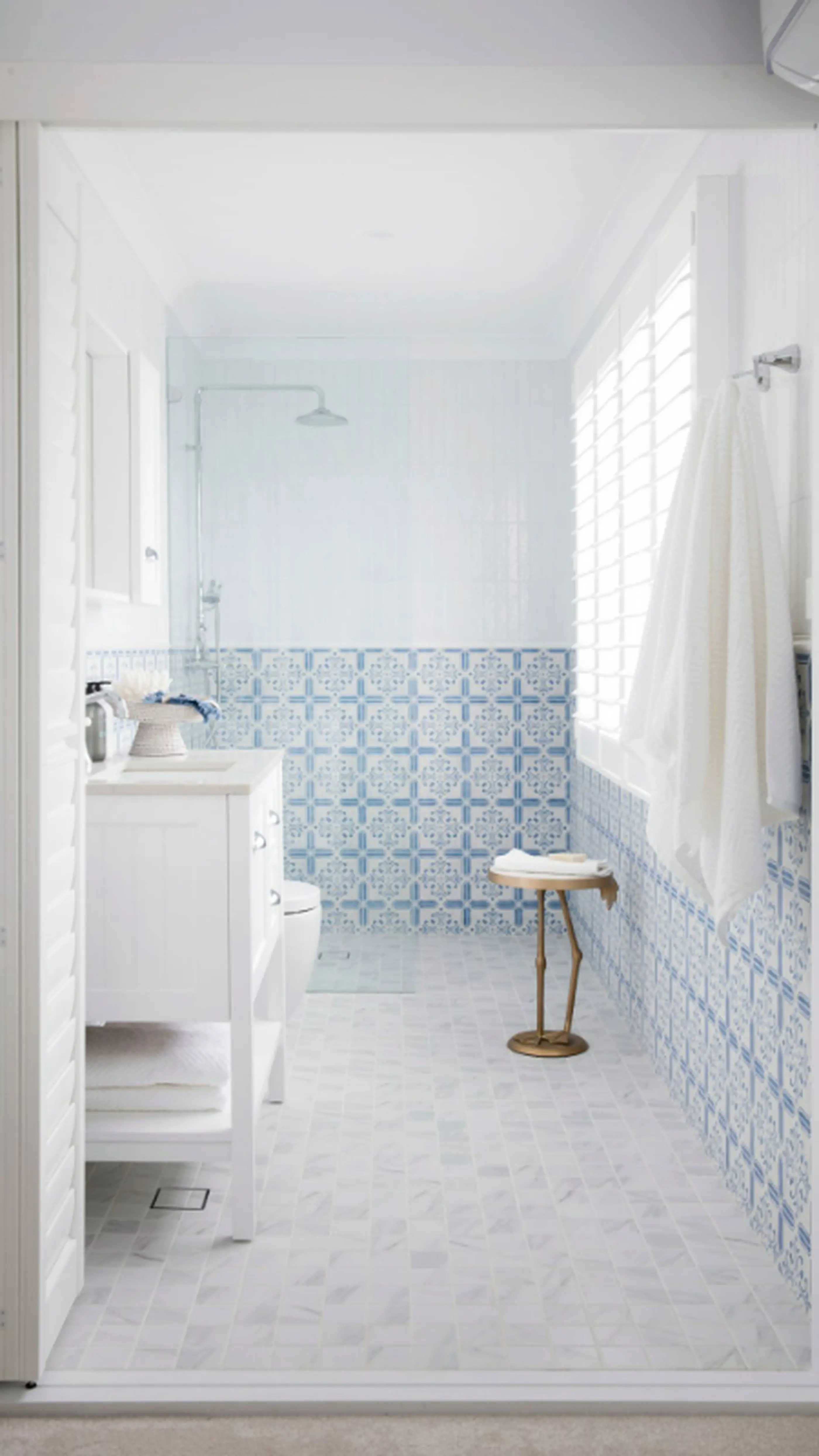Bright bathroom with blue and white patterned tiles, white vanity, walk-in shower, and small wooden stool.