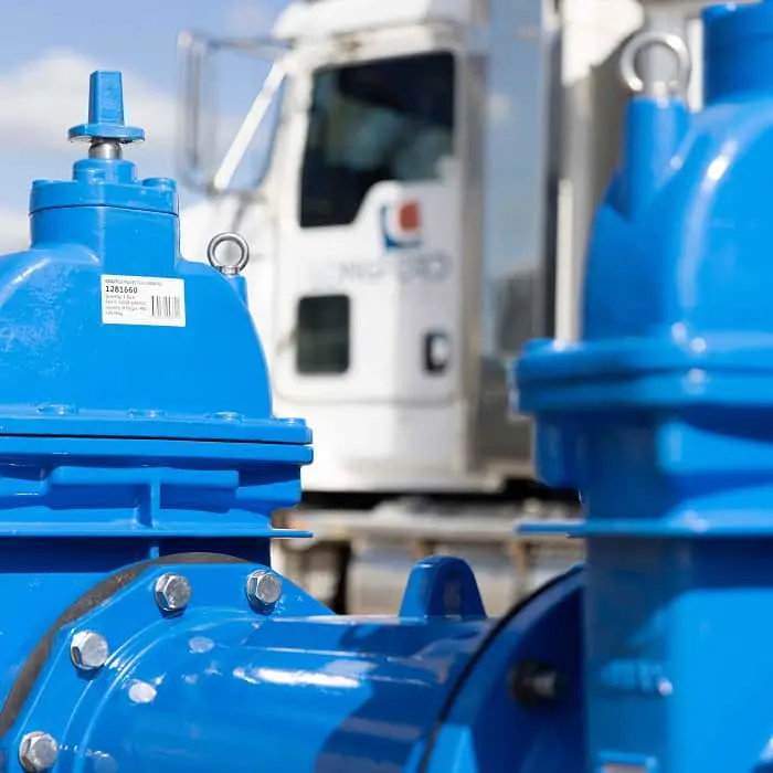 Blue water valves or pipe fittings in foreground with a white service truck visible in the background.