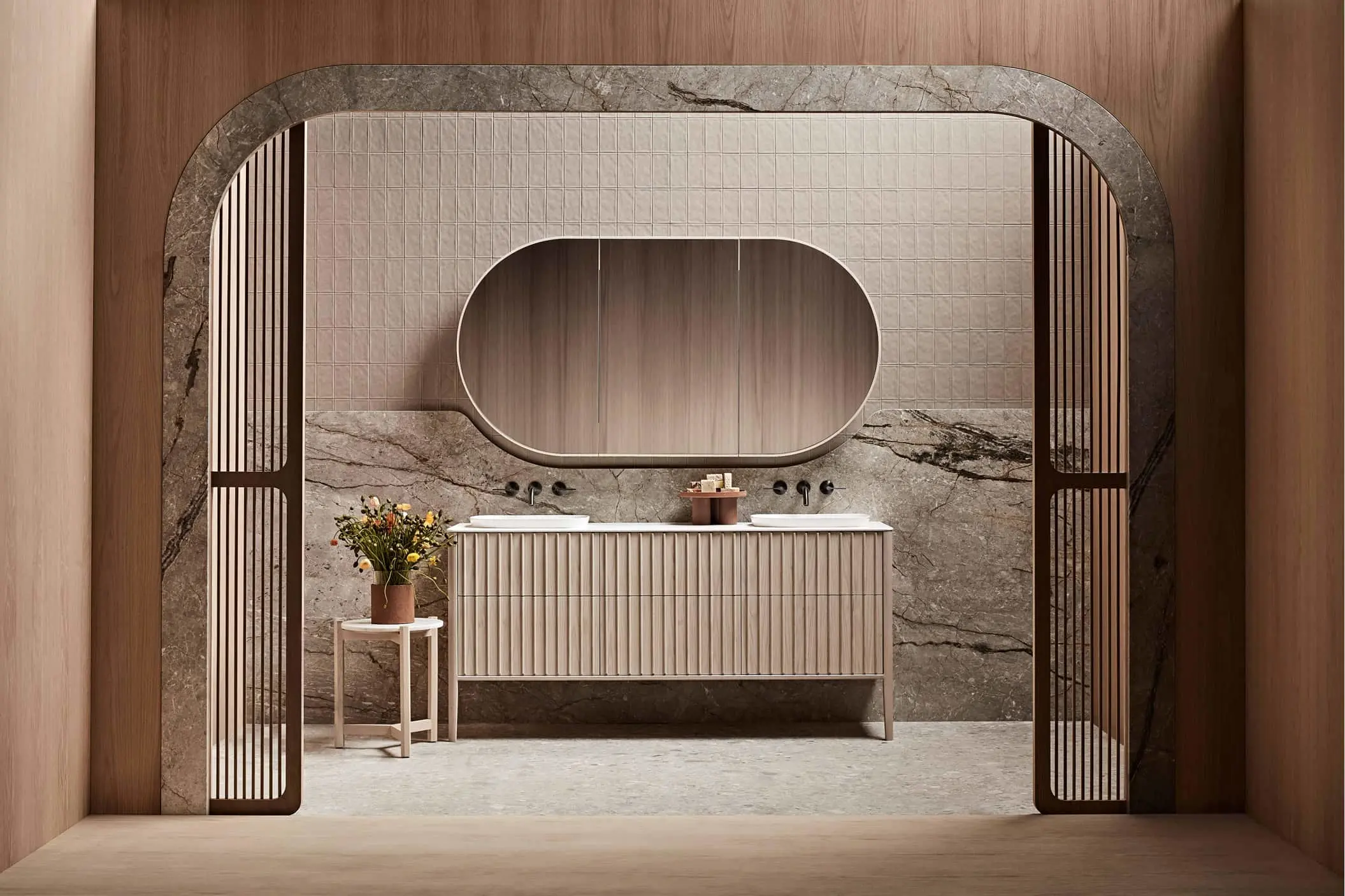 Modern bathroom with marble walls, oval mirror, ribbed vanity cabinet, and small table with flowers viewed through archway.
