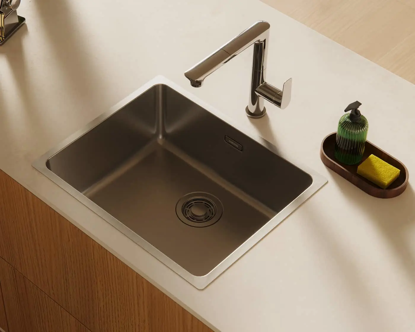 Modern stainless steel kitchen sink with chrome faucet on white countertop, wooden tray with green soap dispenser and yellow sponge.