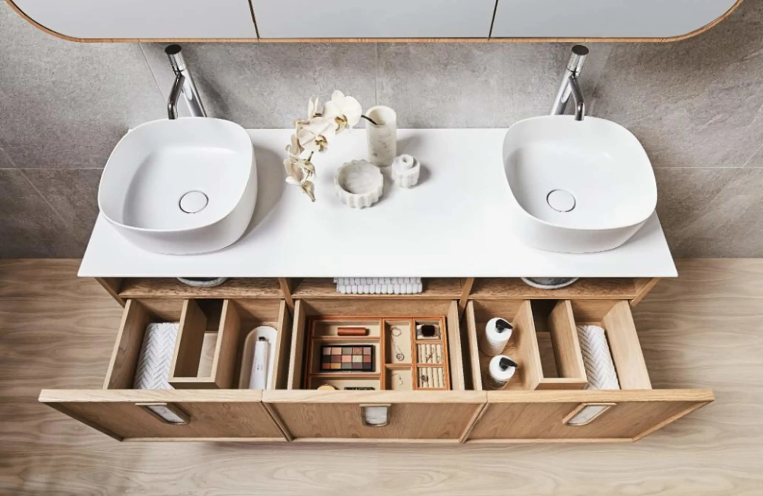 Modern bathroom vanity with dual white sinks, open wooden drawers displaying organised makeup and toiletries.