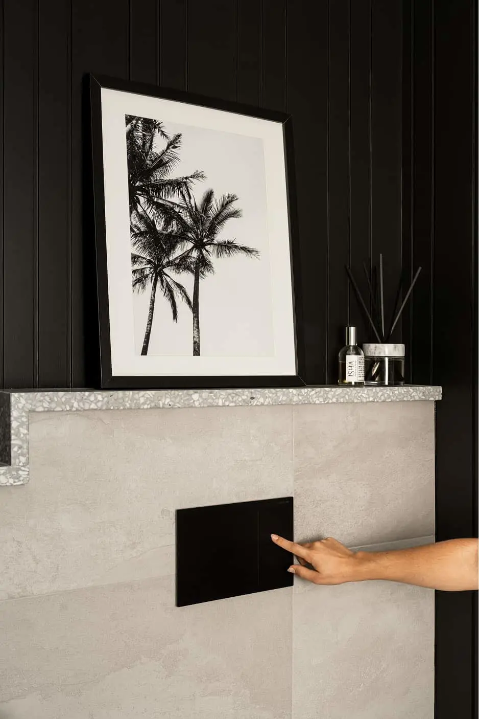 Black and white palm tree artwork in frame on modern stone fireplace mantel with hand touching the fireplace surface.