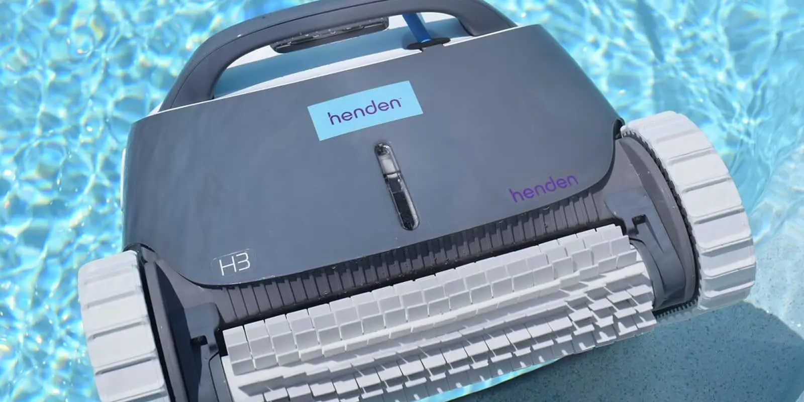 Gray Henden H3 robotic pool cleaner with white wheels floating in blue swimming pool water.
