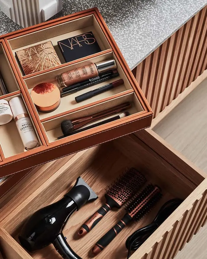 Wooden organizer drawers containing makeup products in top compartment and hair styling tools in bottom drawer.