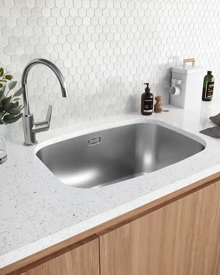 Modern kitchen sink with chrome faucet, white hexagon tile backsplash, and quartz countertop on wood cabinetry.