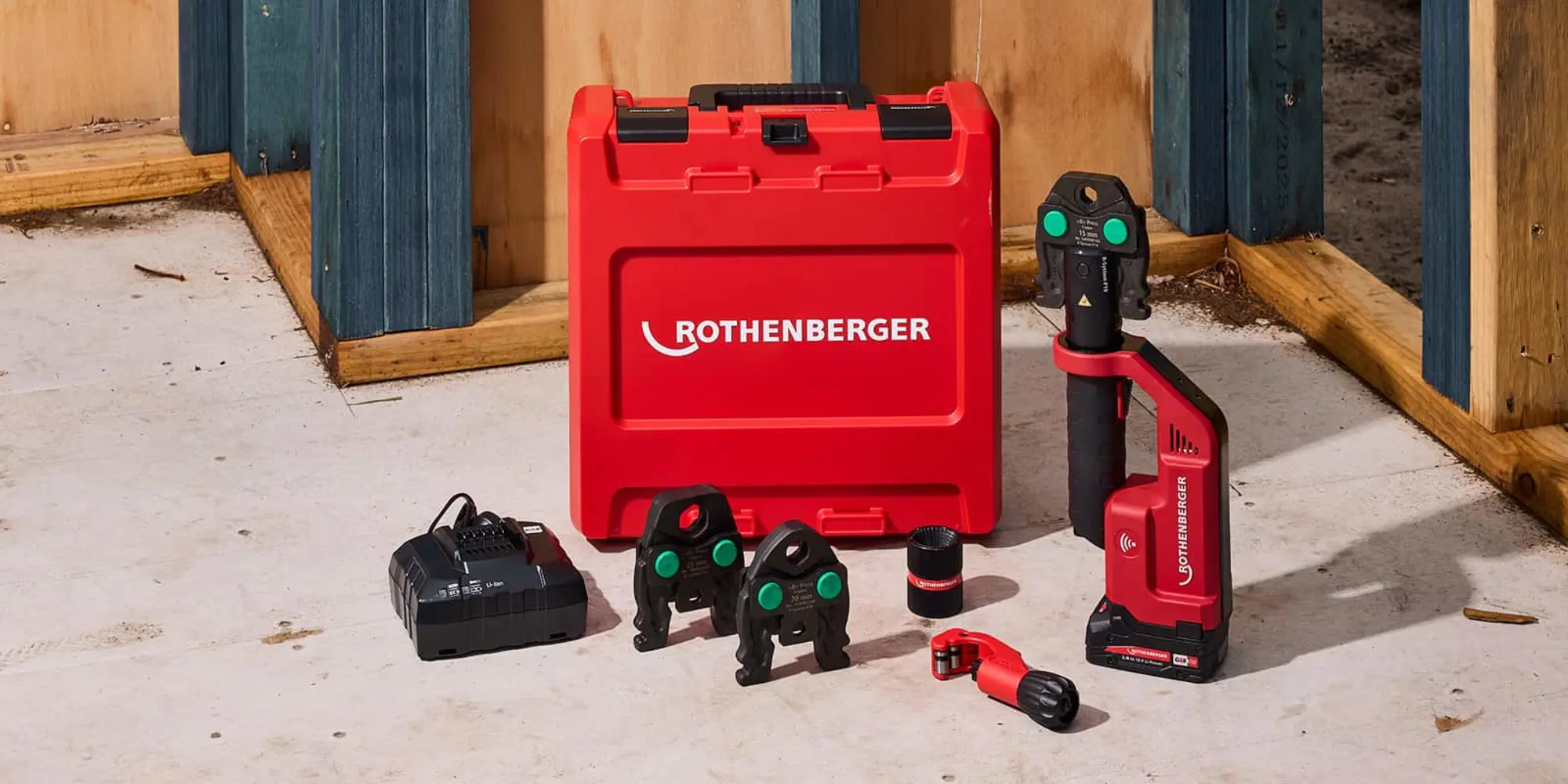 Red Rothenberger tool kit on a concrete floor, including a press tool, jaw attachments, charger, and a red carrying case.