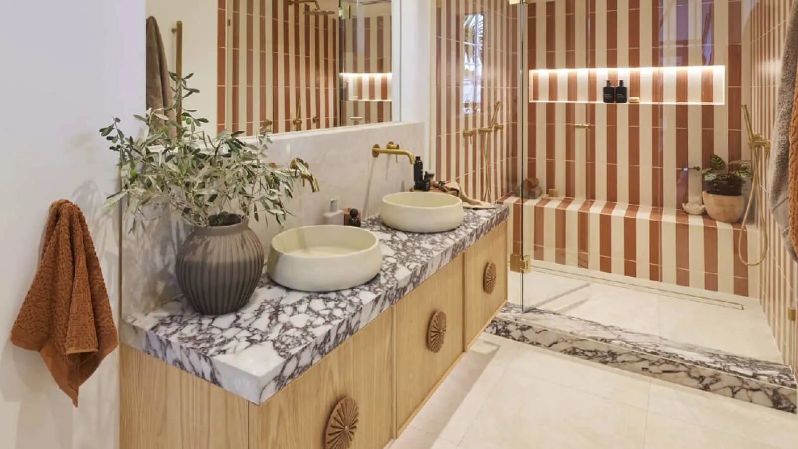 Modern bathroom with marble countertop, two vessel sinks, wooden cabinetry, striped terracotta wall tiles, and potted plant.