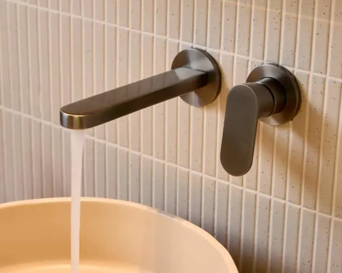 Wall-mounted gunmetal faucet with handle above a white sink against vertical white tile backsplash