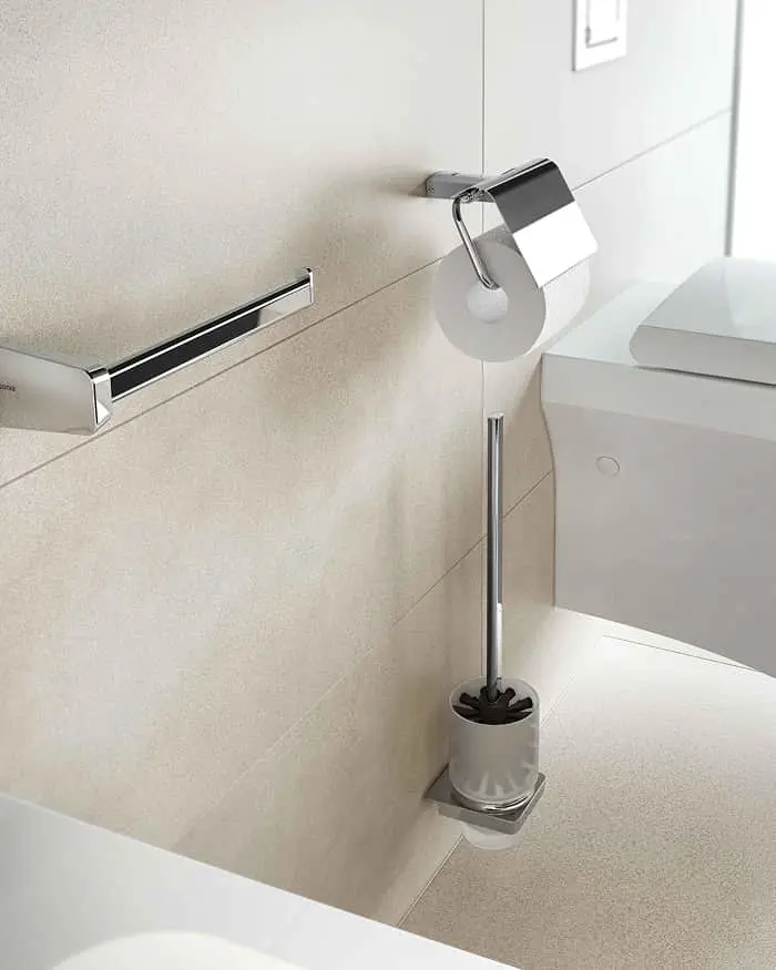 Modern bathroom fixtures including chrome toilet paper holder, toilet brush, and towel bar mounted on beige tiled wall.