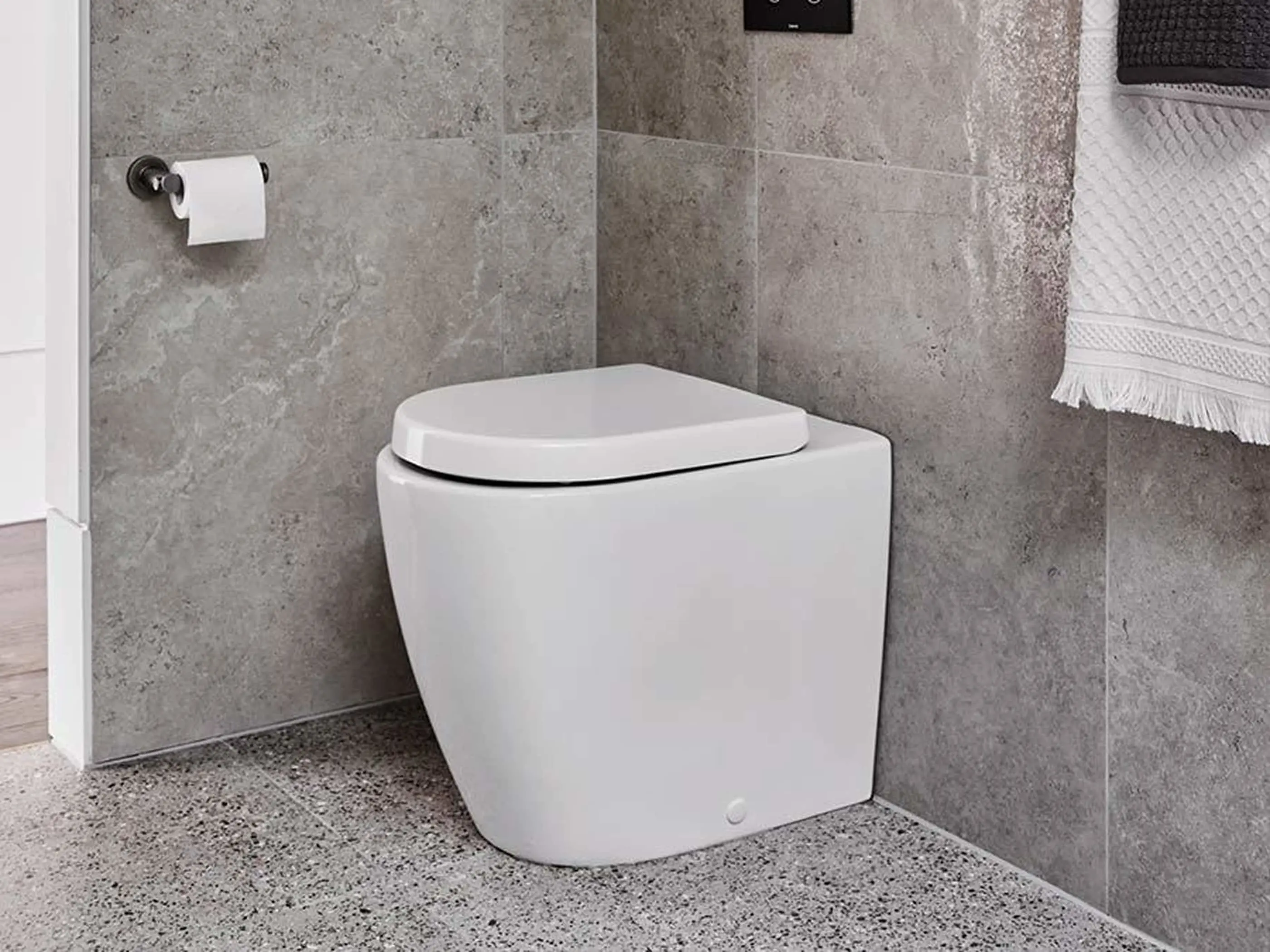 Modern white toilet in bathroom with gray stone tile walls, terrazzo floor, and white towel hanging nearby.