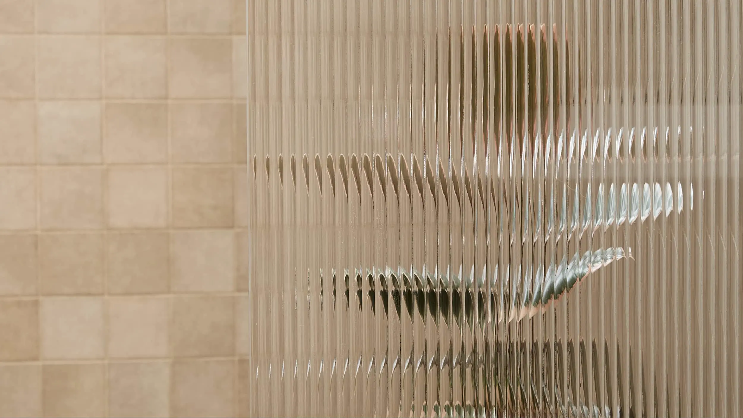 Textured glass shower door with rippled pattern next to beige tiled bathroom wall, creating a distorted view.