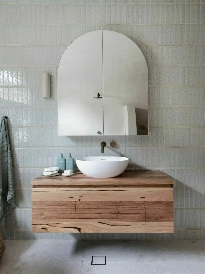 Modern bathroom with arch-shaped mirror cabinet, white vessel sink on floating wooden vanity, and pale blue tiled walls.