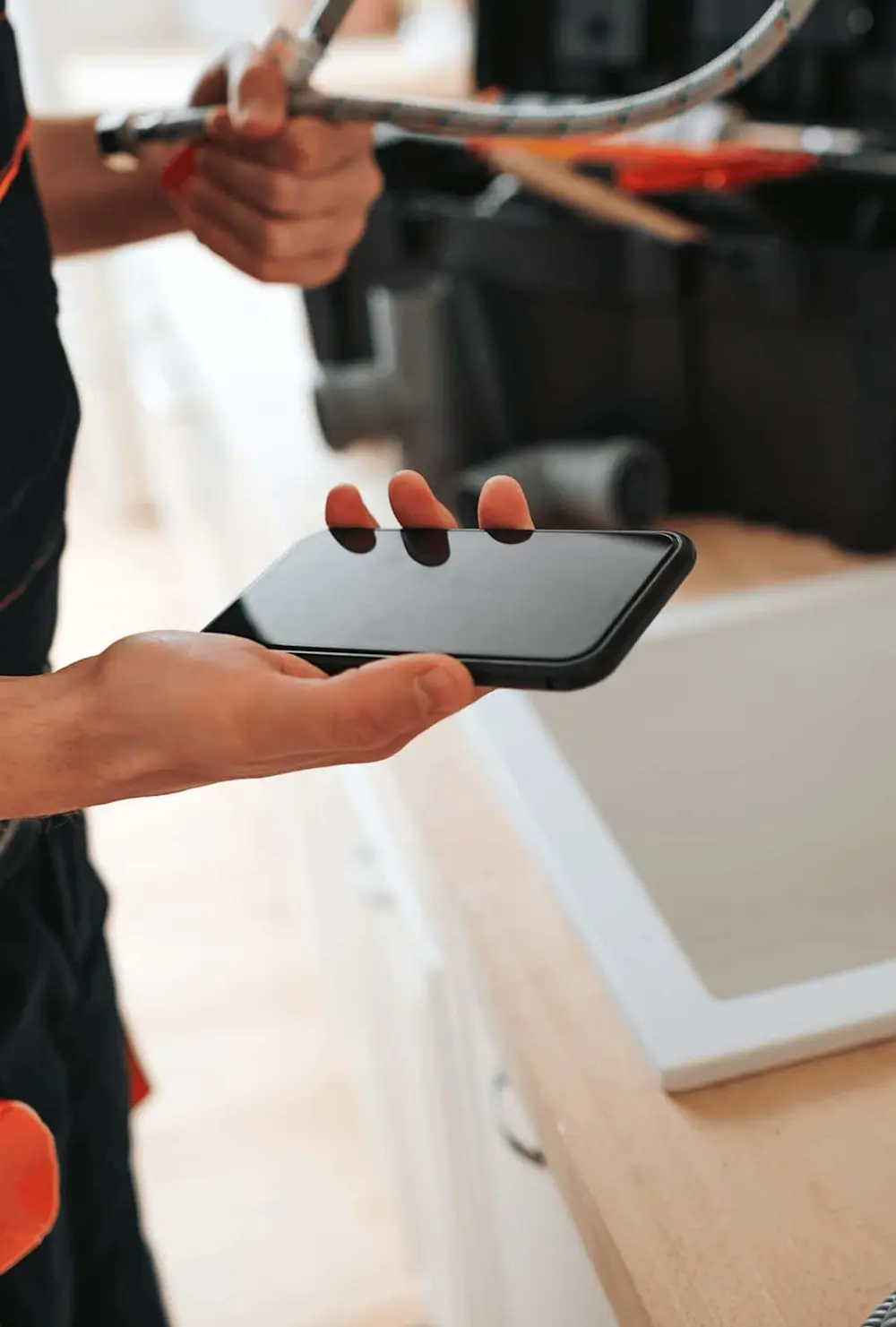 Person holding smartphone while working with tools, possibly doing home repairs or installation work.
