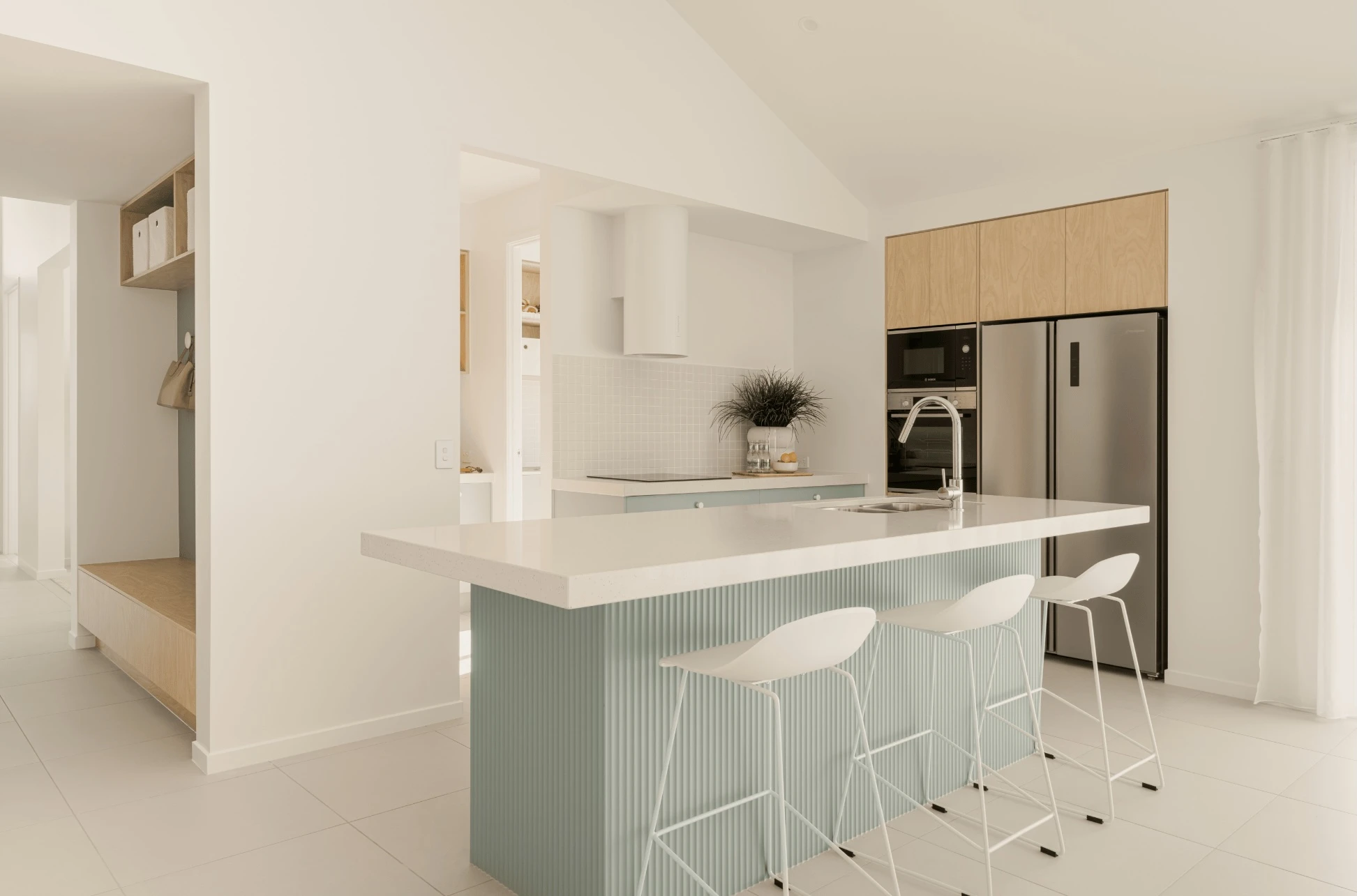 Modern kitchen with mint green island, white countertops, stainless steel appliances, and three white bar stools.