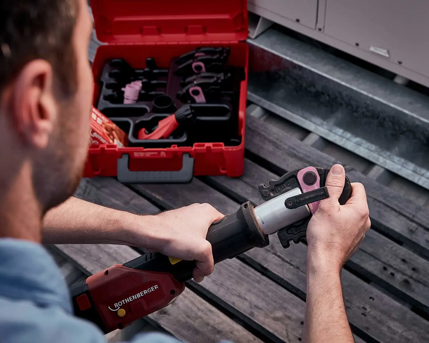 Person using a Rothenberger power tool with an open red toolbox containing various tools nearby on wooden decking.