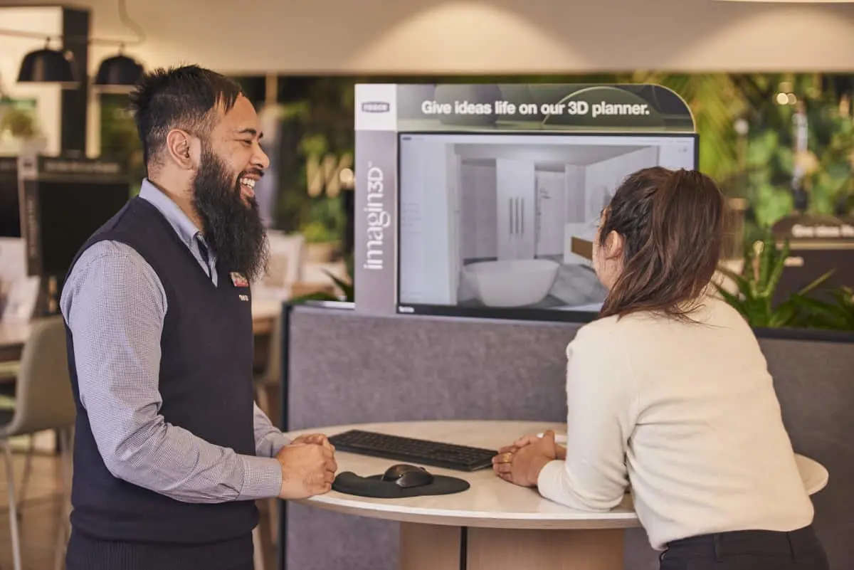 Bathroom consultant helping customer use 3D bathroom planner at a design station in a showroom.