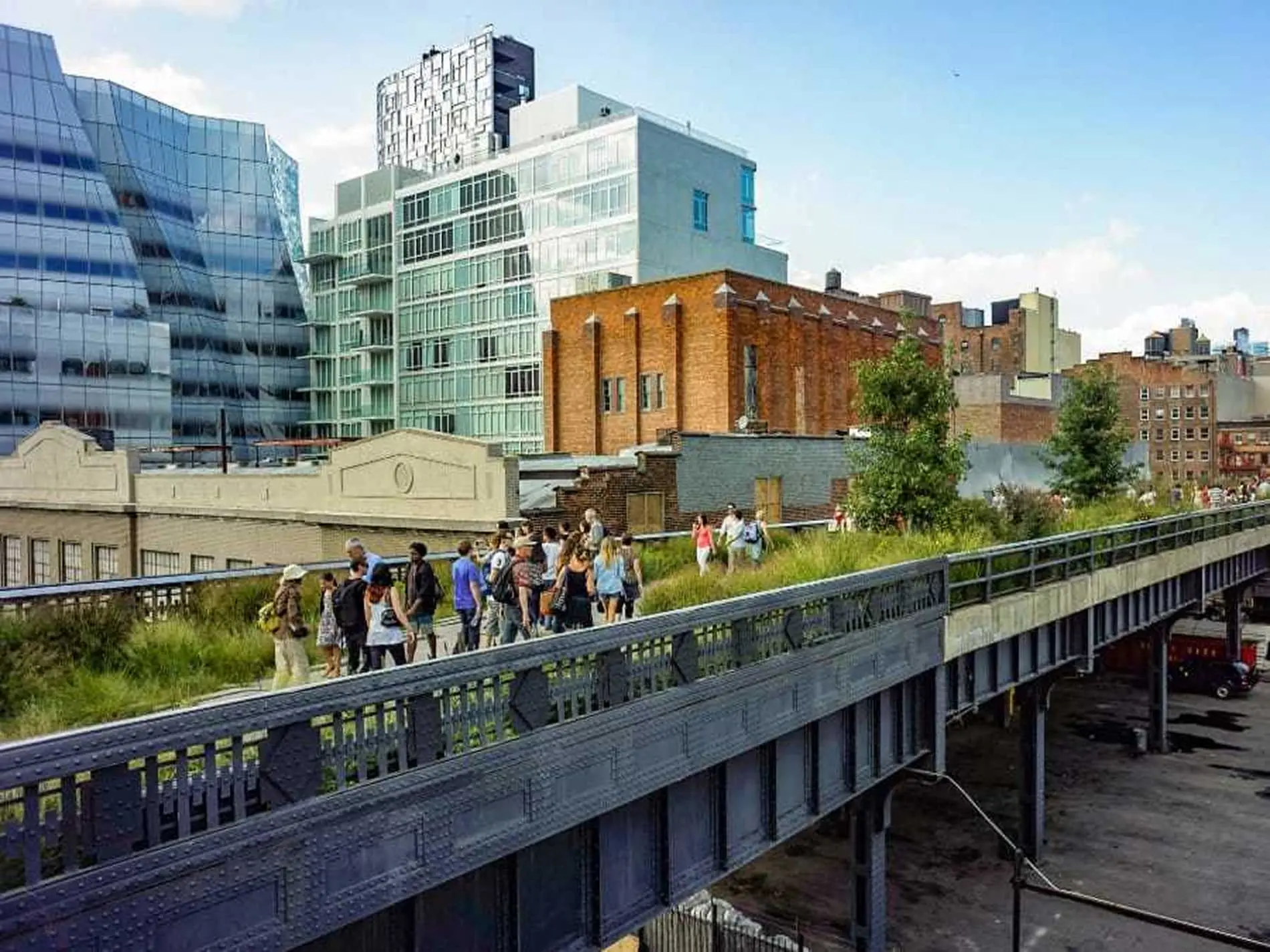 People walking along the High Line elevated park with modern and historic buildings in the background.