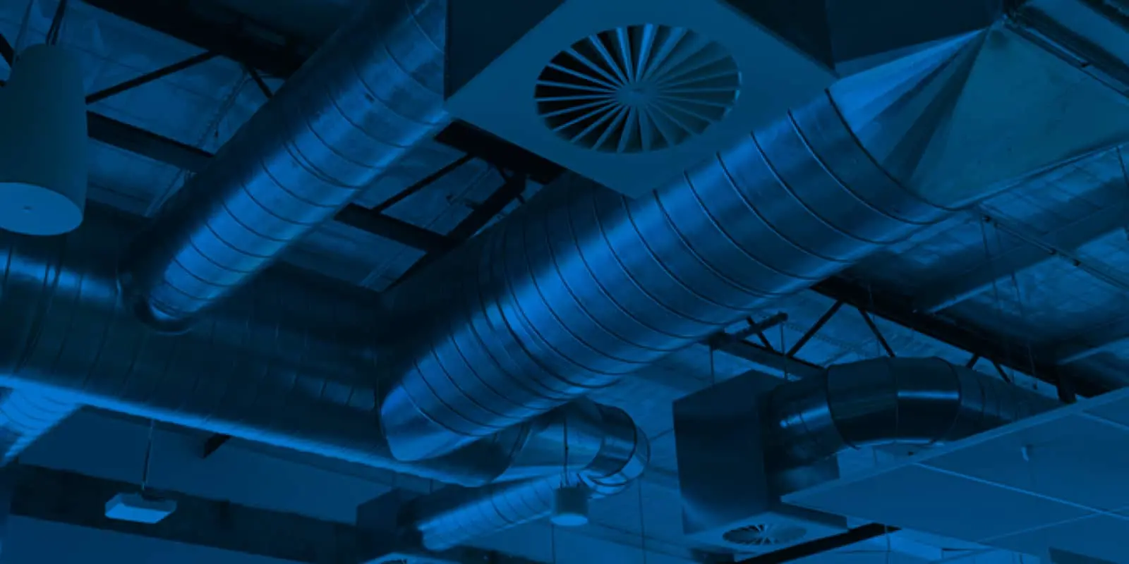 Industrial ventilation system with metal ductwork and circular vents illuminated in blue lighting.