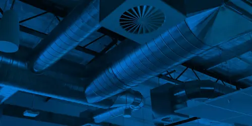 Industrial ventilation system with metal ductwork and circular vents illuminated in blue lighting.