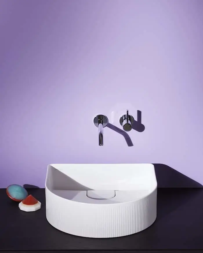 Modern white basin sink with wall-mounted chrome faucet on dark countertop against purple wall.