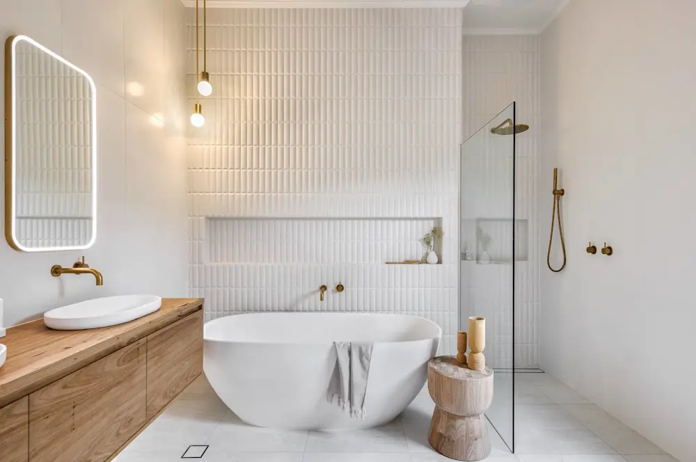 Modern white bathroom with freestanding tub, wooden vanity, gold fixtures, and glass shower enclosure.