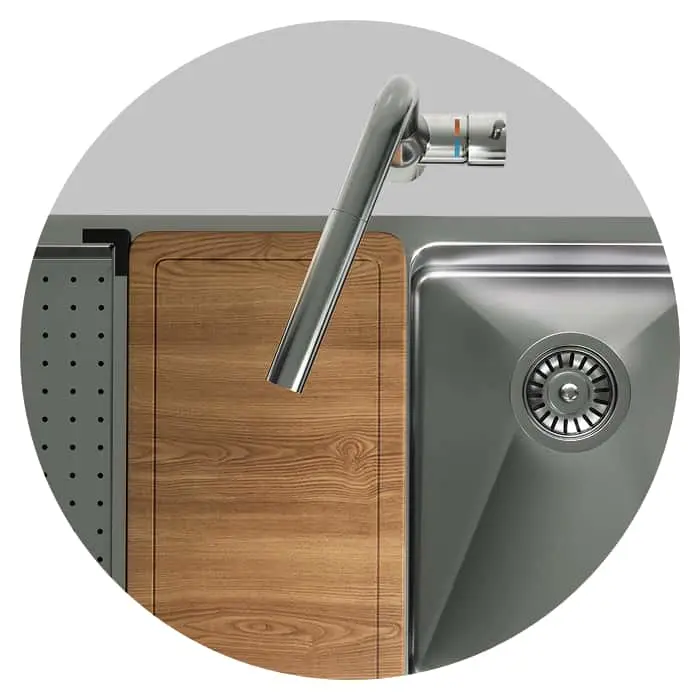 Modern kitchen sink with stainless steel faucet, wooden cutting board, and metal drain in circular frame view.