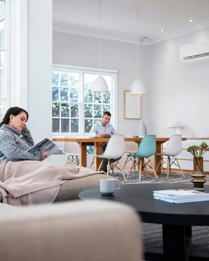 Bright modern living space with person reading on couch while another works at wooden table with colorful chairs.