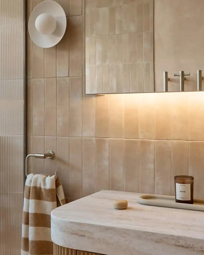 Modern bathroom with beige tiled walls, marble sink, striped towel, wall sconce, and candle on countertop.
