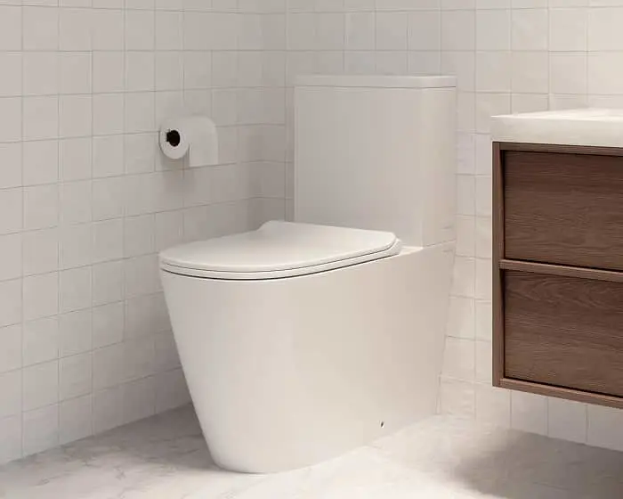 Modern white toilet in a bathroom with white tiled walls, toilet paper holder, and wooden cabinet visible.
