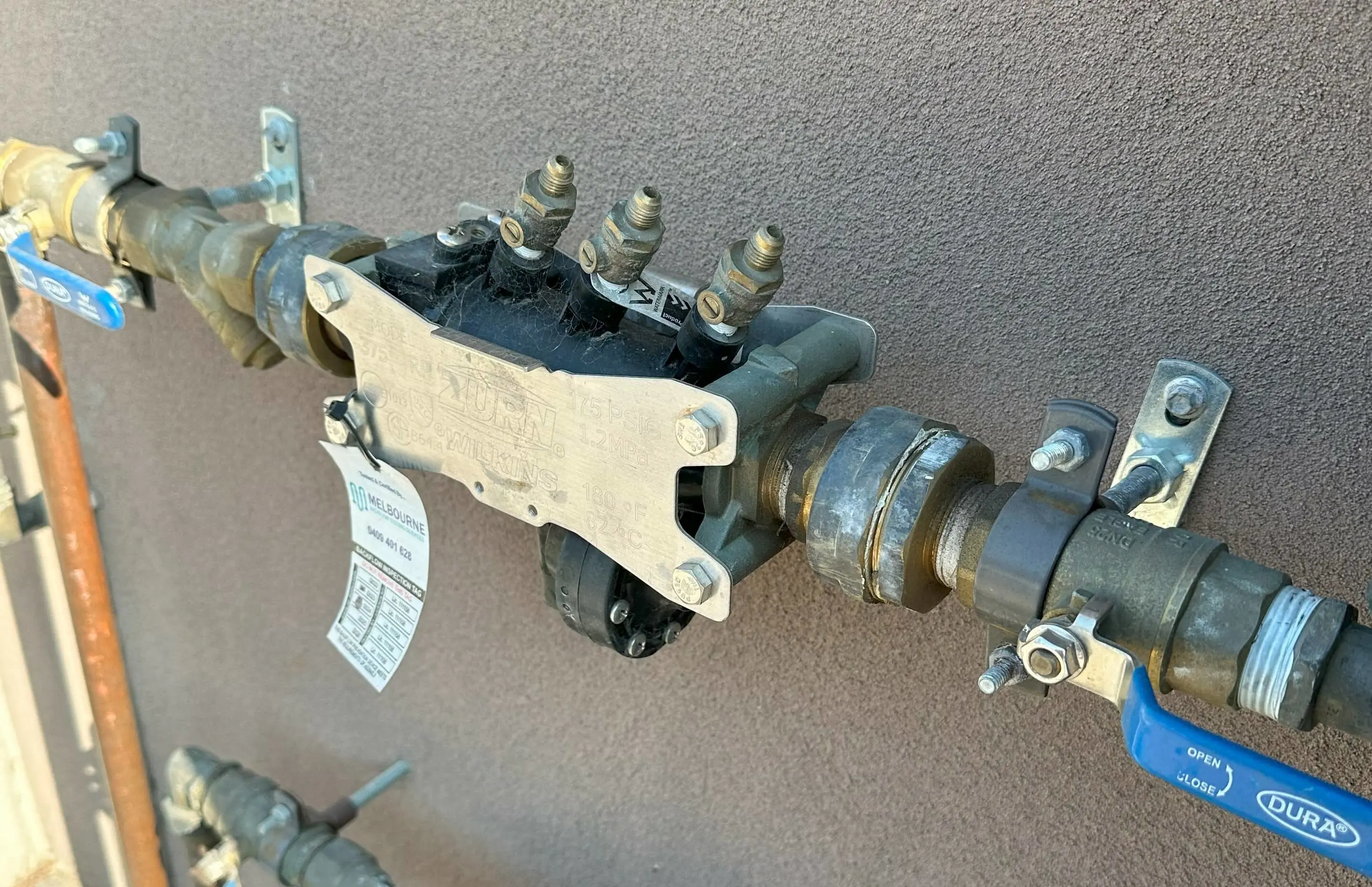 Water pipe assembly with blue valve handle and metal fittings mounted on gray wall.