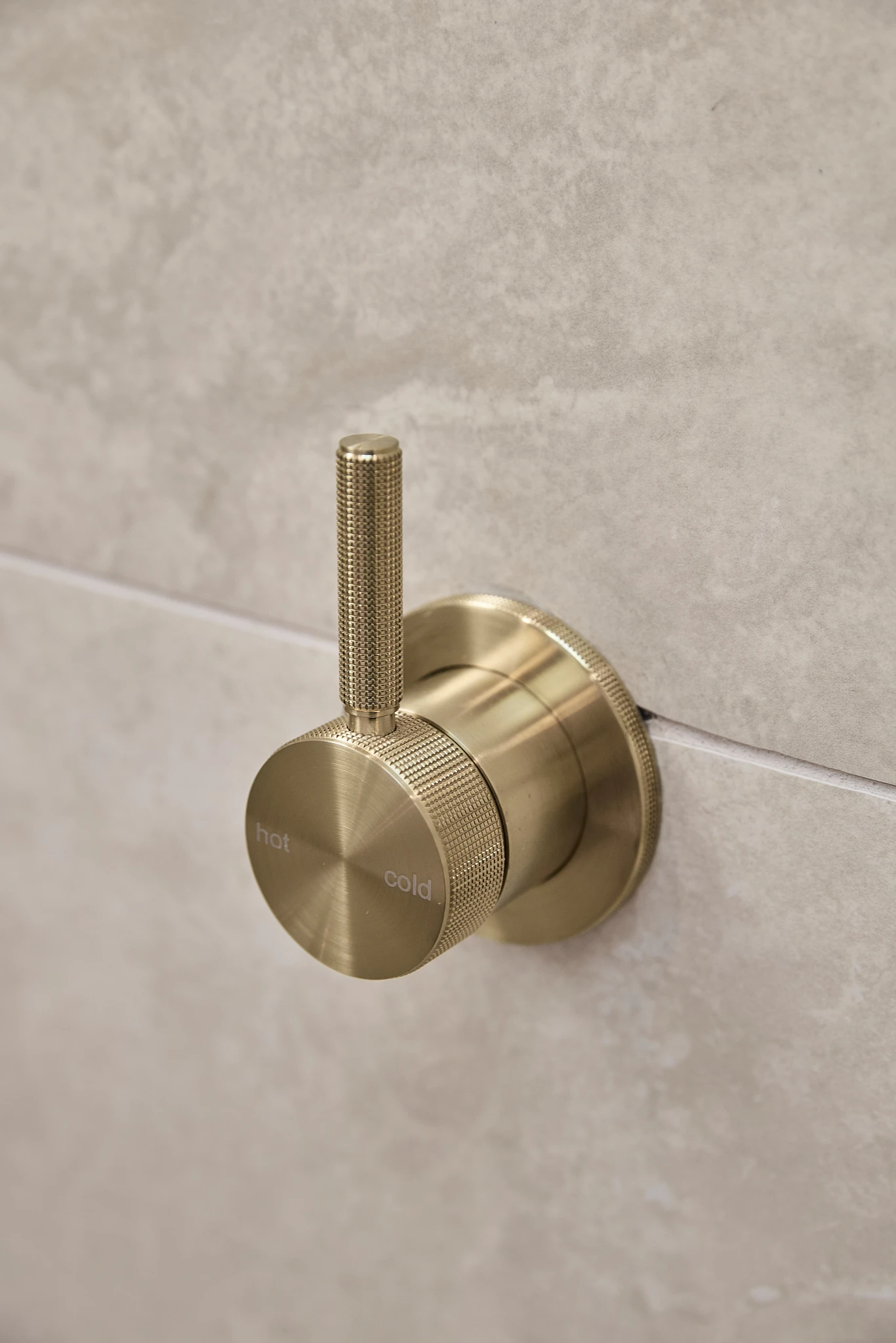Brass bathroom faucet handle with hot and cold markings mounted on a light beige stone wall.