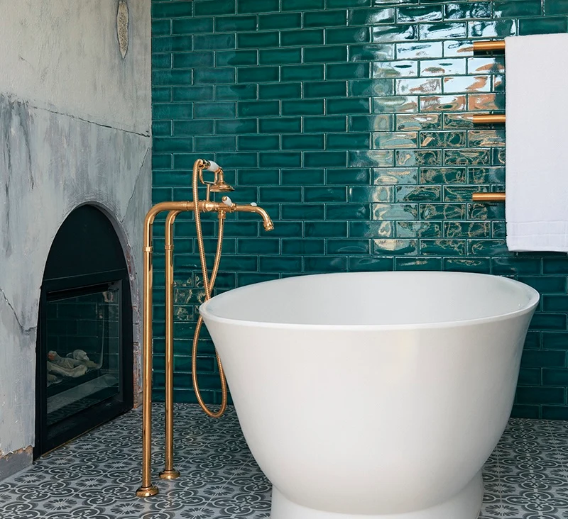 Modern bathroom with white freestanding tub, brass faucet fixture, and glossy teal subway tile wall.