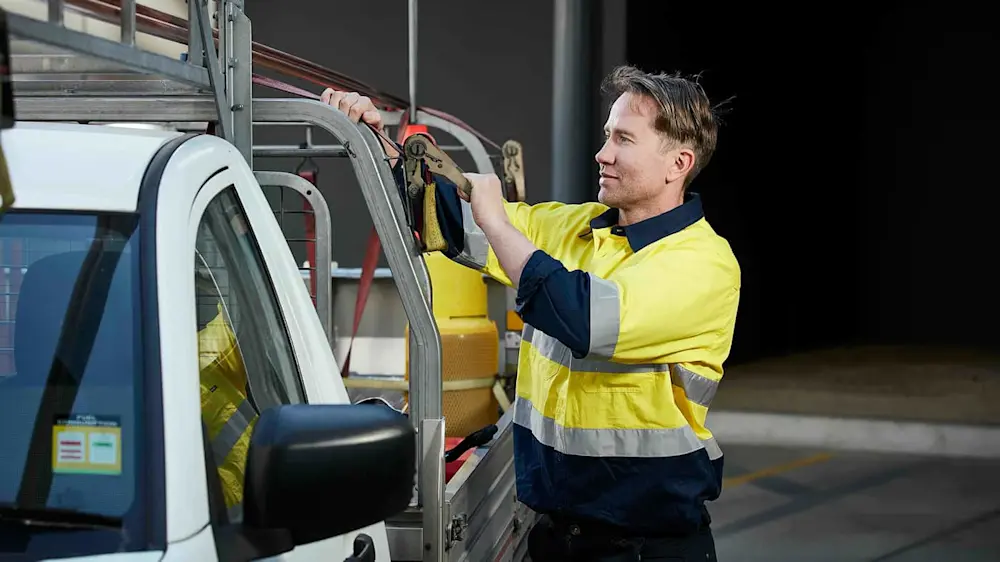 Worker in high-visibility yellow shirt using tools to secure equipment on a white service vehicle.