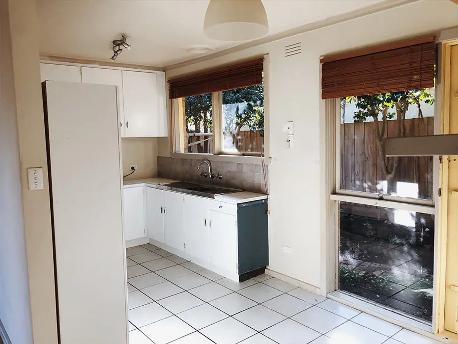 Small kitchen with white cabinets, tiled floor, wooden blinds, and glass door leading to backyard with fence.