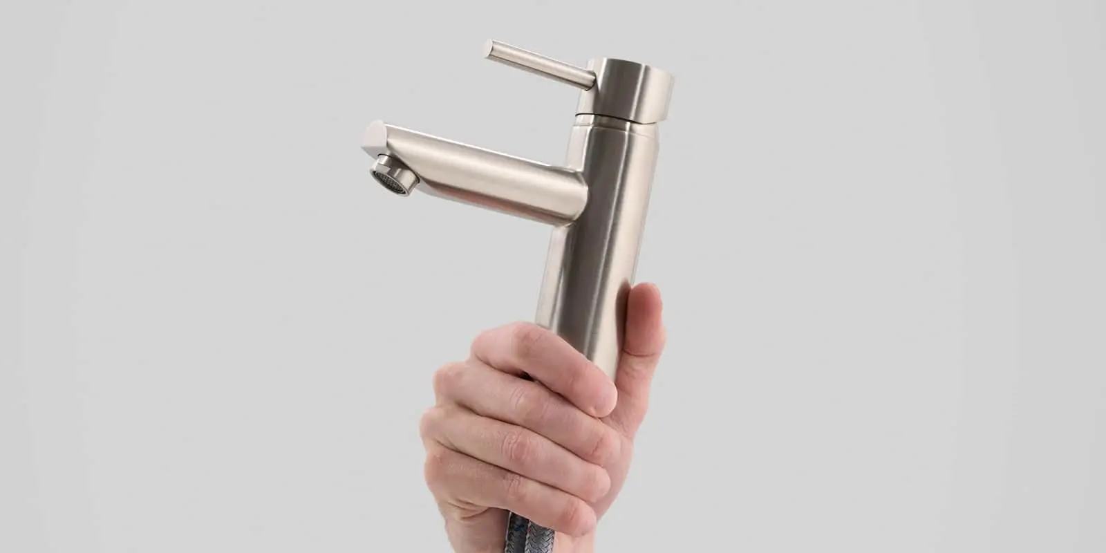 Hand holding a stainless steel bathroom faucet against a light gray background.