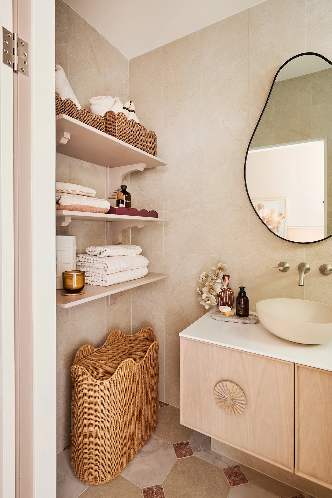 Bathroom with open shelves holding towels and baskets, a wicker hamper, wood vanity with vessel sink, and round mirror.
