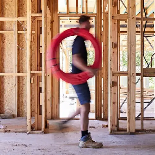 Blurred worker carrying red coil through wooden house frame under construction