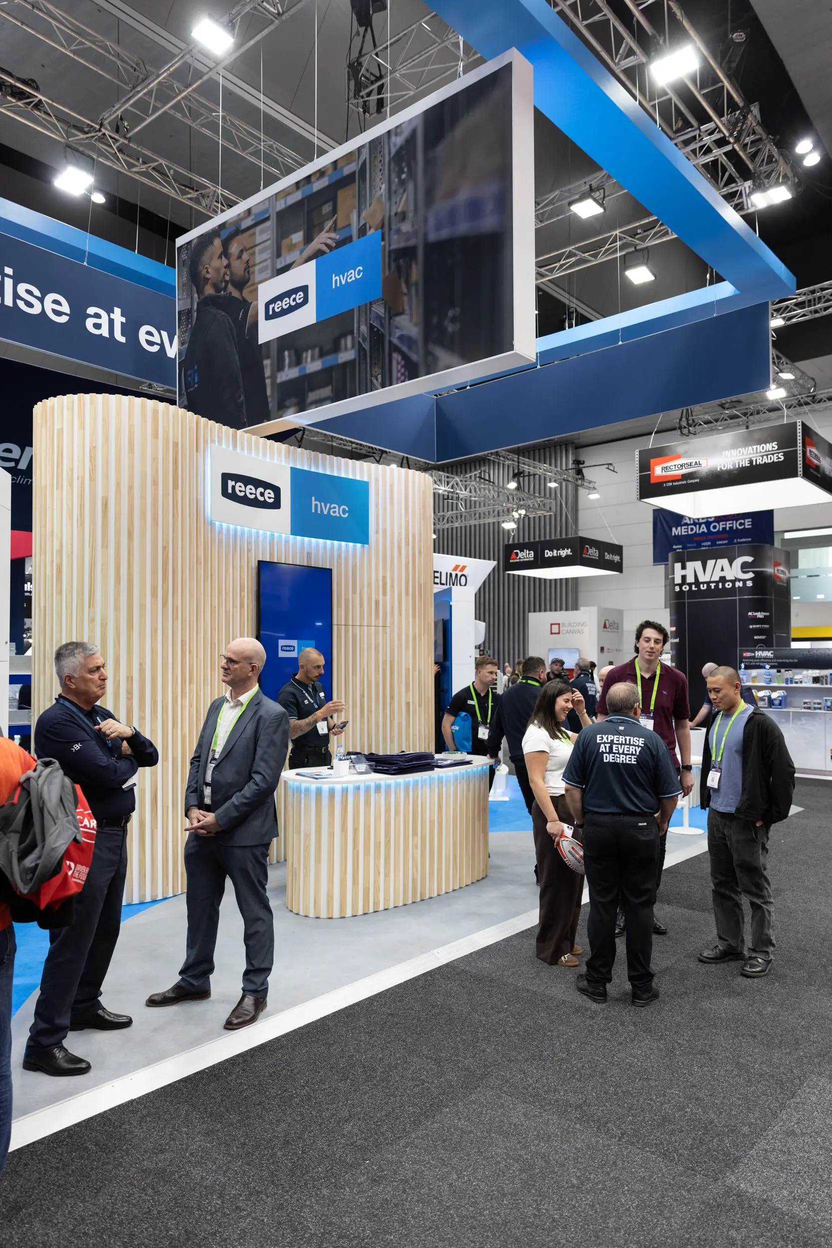 People gathered at the Reece HVAC exhibition booth with wood-slat design at a trade show.