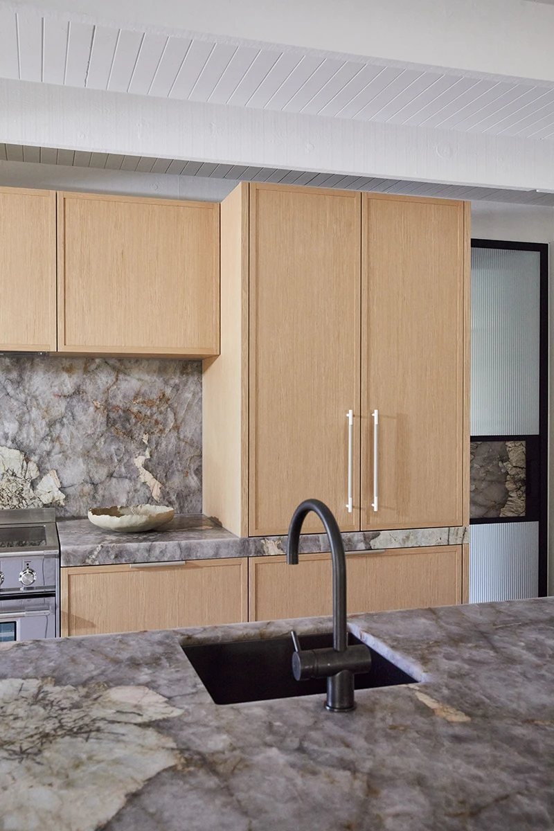 Modern kitchen with light wood cabinets, marble countertops and backsplash, black sink and faucet, and white ceiling.
