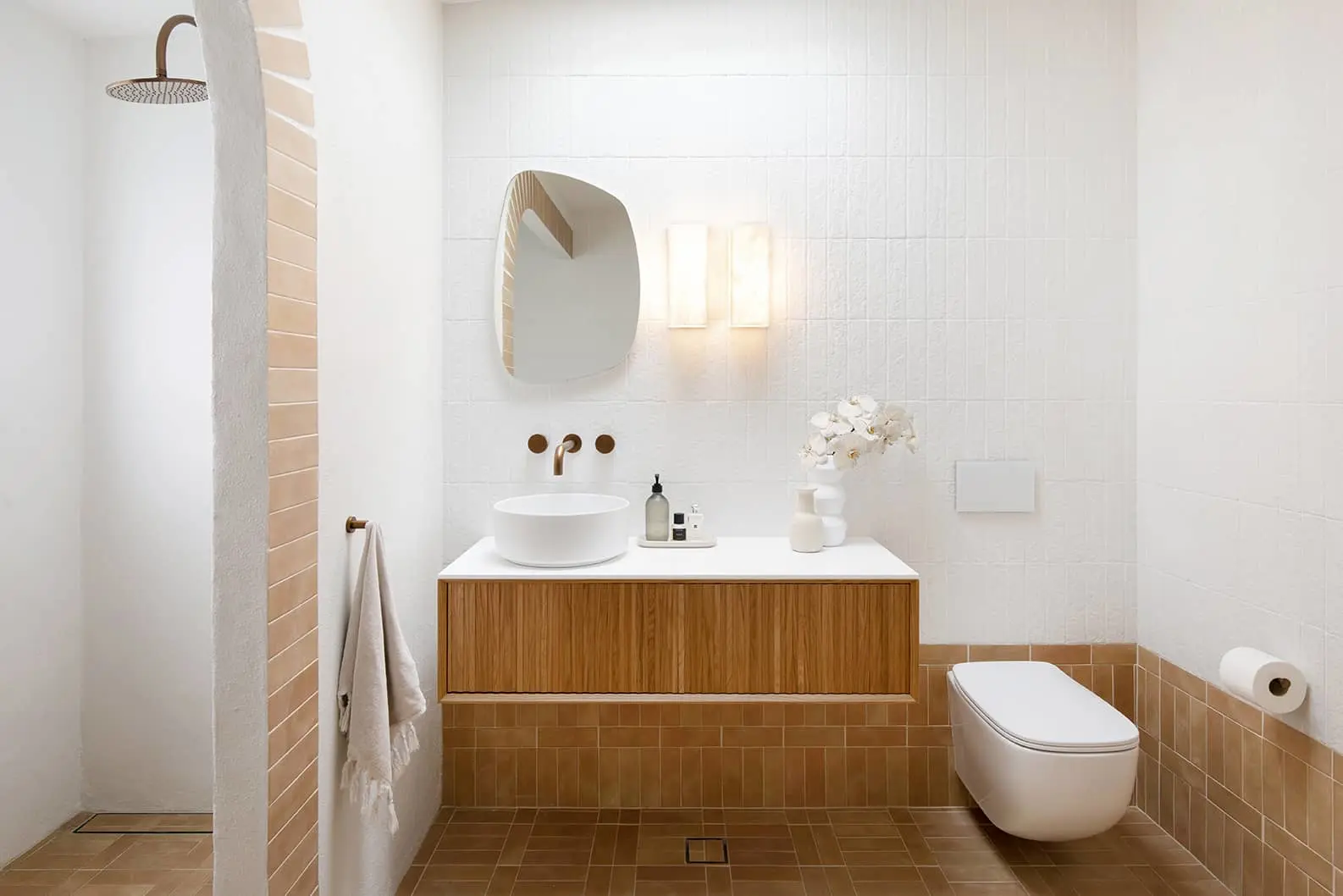 Modern bathroom with white and terracotta tiles, wooden vanity, round mirror, rainfall shower, and white toilet.