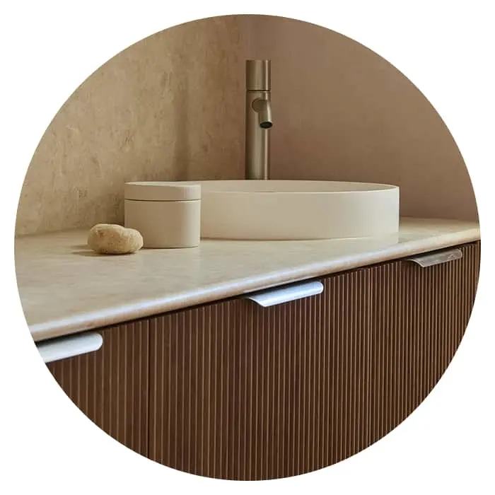 Modern bathroom vanity with cream oval sink, brass faucet, and ribbed wooden cabinetry beneath marble countertop.