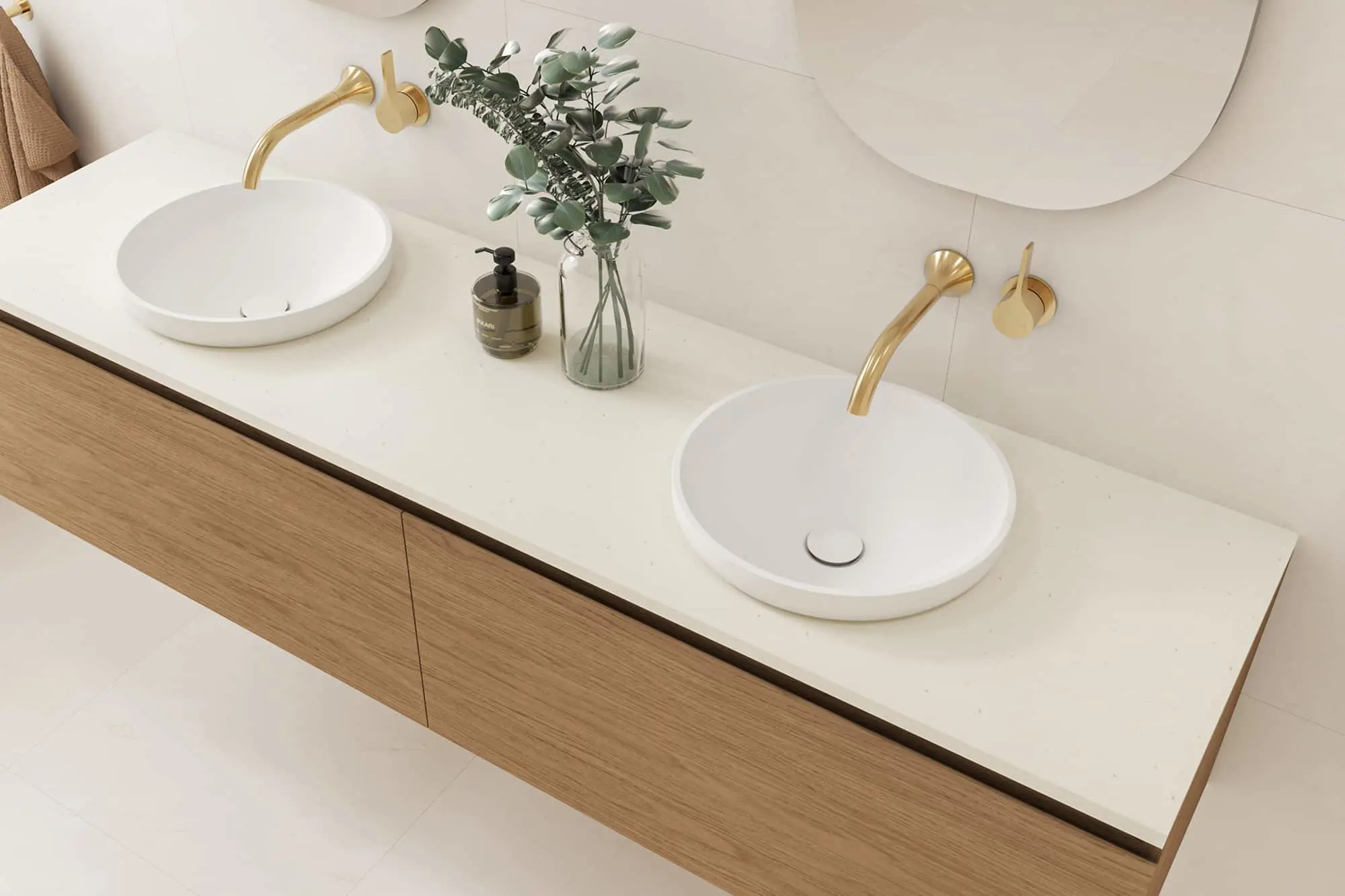 Modern bathroom vanity with dual white vessel sinks, brass faucets, wooden cabinet, and eucalyptus in glass vase.