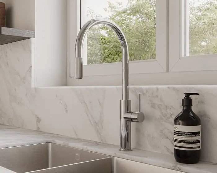 Chrome pull-down kitchen faucet on a marble countertop near a window, with a dark soap dispenser beside it.