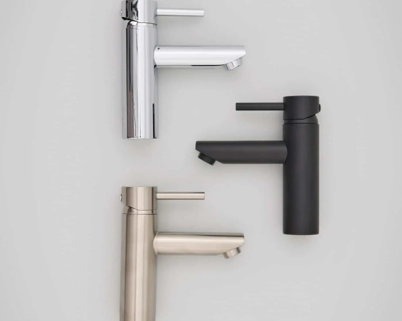 Three bathroom faucets in chrome, black, and brushed nickel finishes arranged on a white surface.