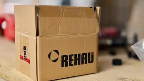 Open brown cardboard box with REHAU logo on a wooden surface, blurred background.
