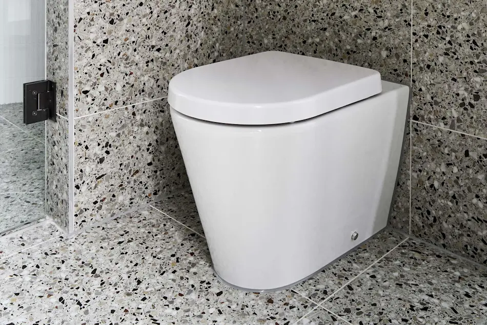 White toilet with closed lid in bathroom corner with speckled terrazzo-style walls and flooring.