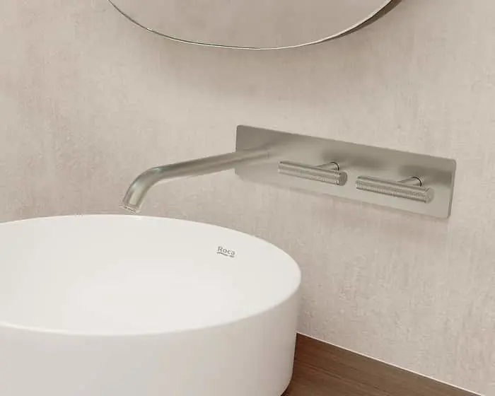 Modern bathroom sink with wall-mounted brushed steel faucet and white oval basin by Roca.