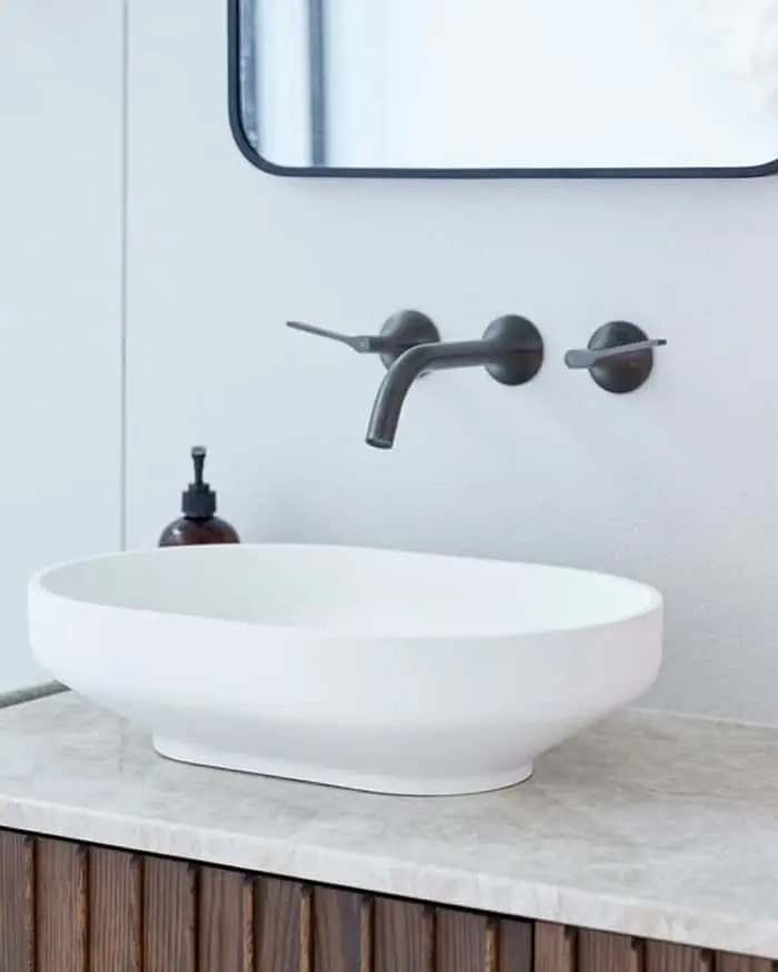 Modern bathroom with white vessel sink, wall-mounted black faucet, marble countertop, and wooden vanity cabinet.