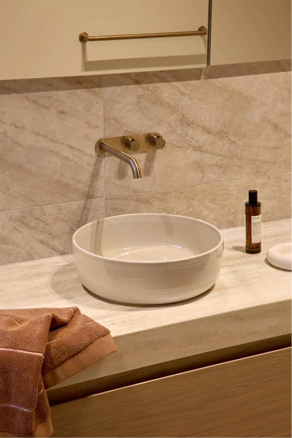 White round vessel sink on marble countertop with brass wall-mounted faucet and mirror above